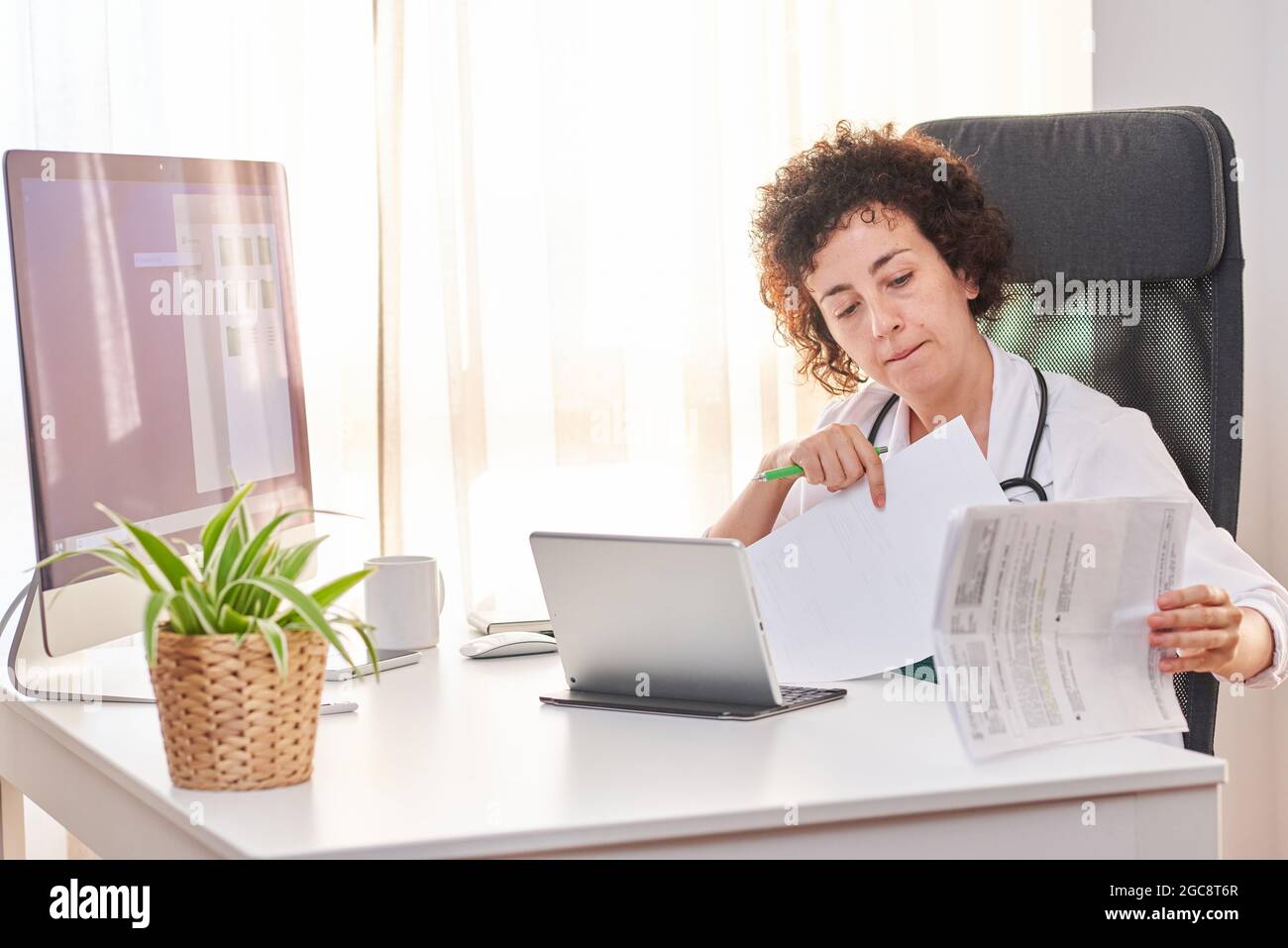 Donna medico digitalizzare i documenti attraverso il suo tablet seduto nel suo ufficio Foto Stock