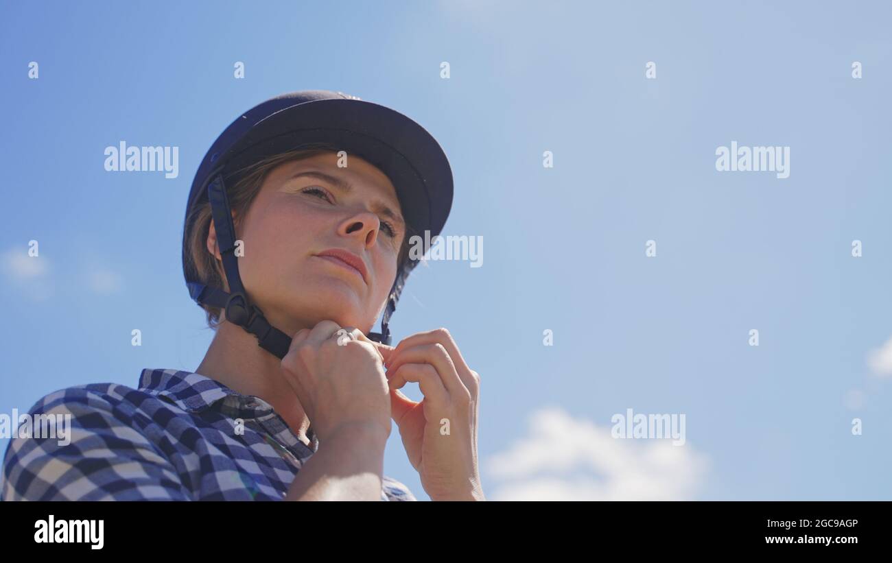 giovane donna cavaliere regola la cintura del casco prima di andare a cavallo. Foto di alta qualità Foto Stock