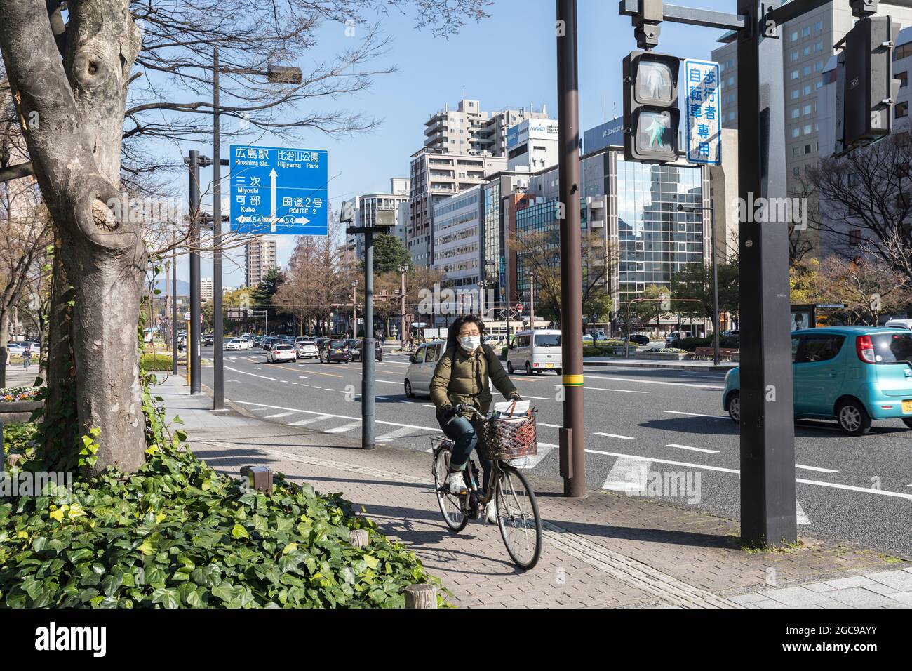 Donna che indossa la maschera in bicicletta sulla pista ciclabile, Hiroshima, Giappone Foto Stock