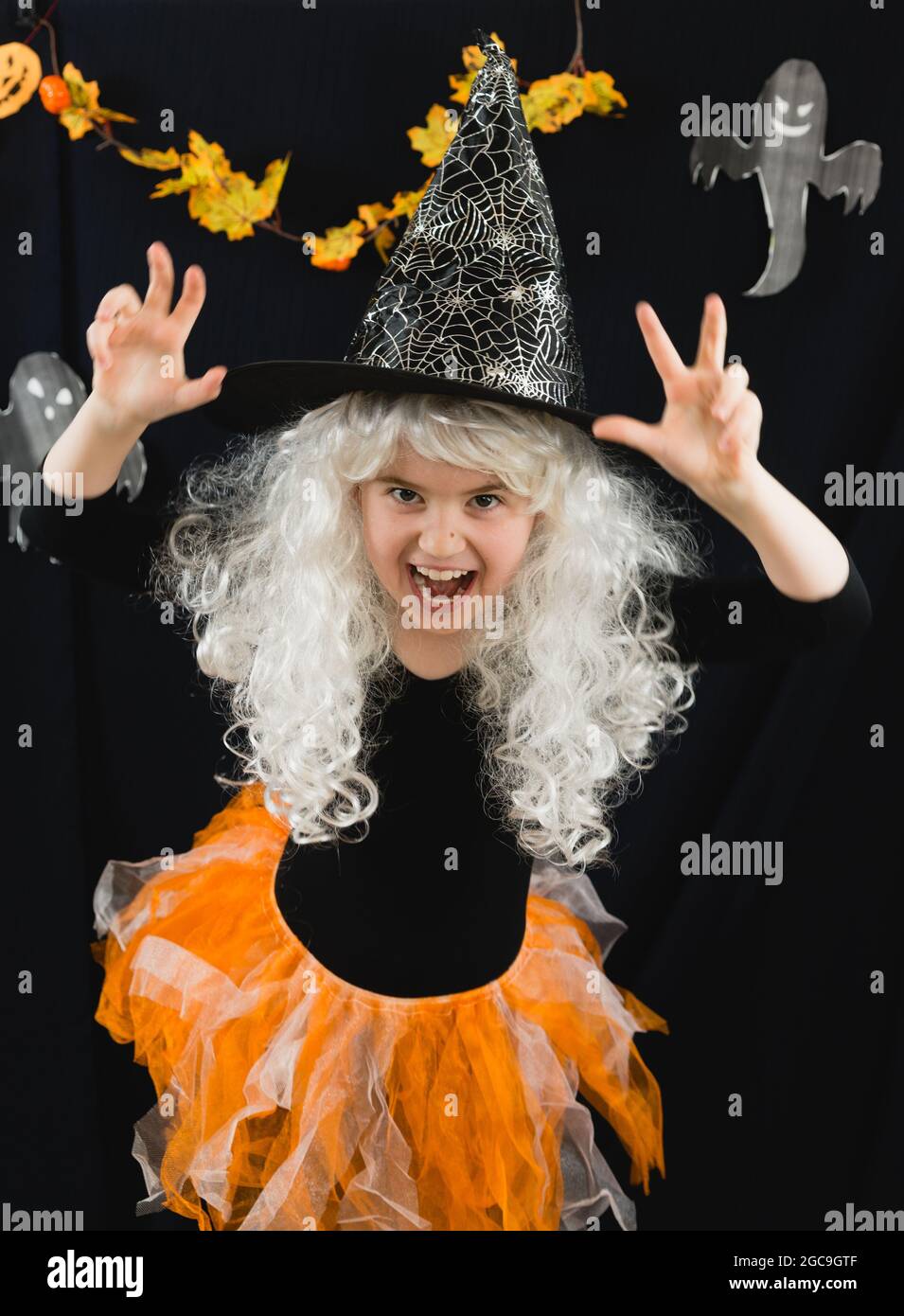 Una ragazza allegra in una parrucca bianca e un costume di strega spaventa. Orrore. Sullo sfondo, un divertente fantasma Casper Foto Stock