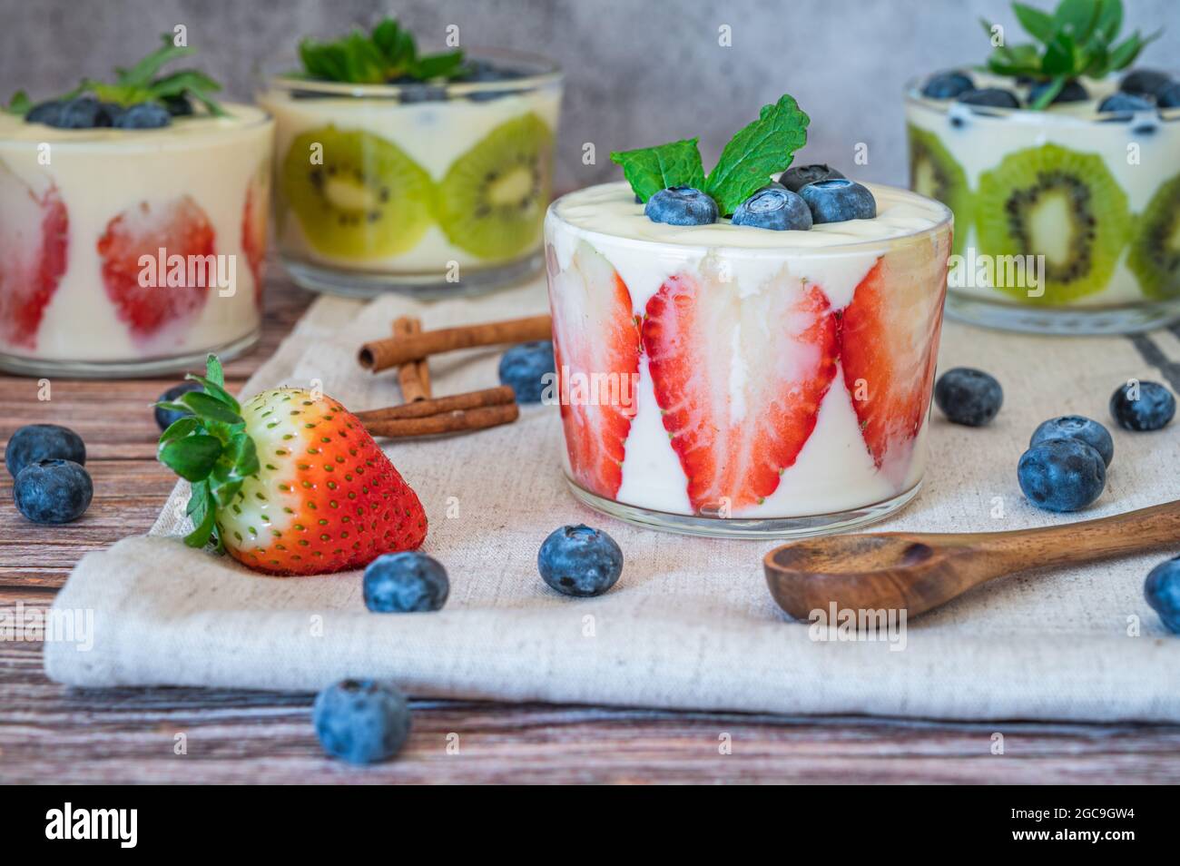 Una sana colazione fatta in casa in un bicchiere con frutta fresca: kiwi, fragola e yogurt su sfondo di legno. Profondità di campo bassa con foc selettivo Foto Stock