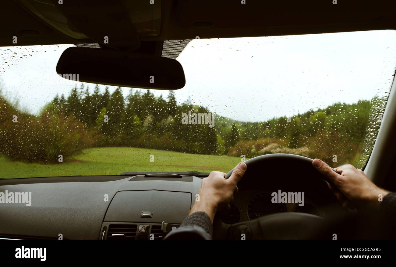 Guida di un moderno fuoristrada guida a destra RHD auto sulla montagna verde foresta di campagna strada in un giorno di pioggia moody. Vista sul parabrezza dell'auto POV Foto Stock