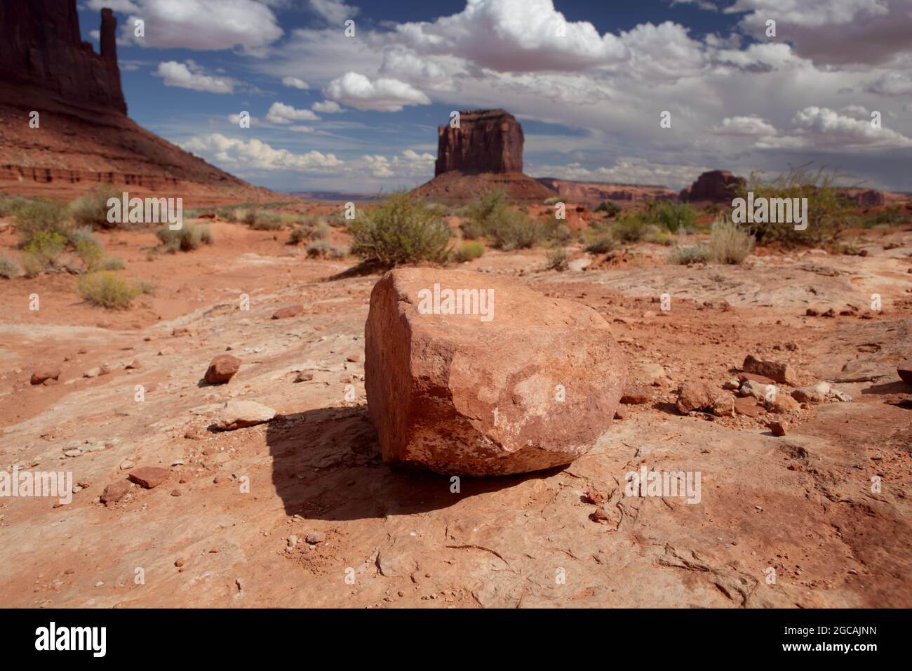 Red Sandstone West Mitten Butte e Merrick Butte scogliere nel Monument Valley Navajo Tribal Park con un masso in primo piano sul Wildcat Escursionismo Foto Stock