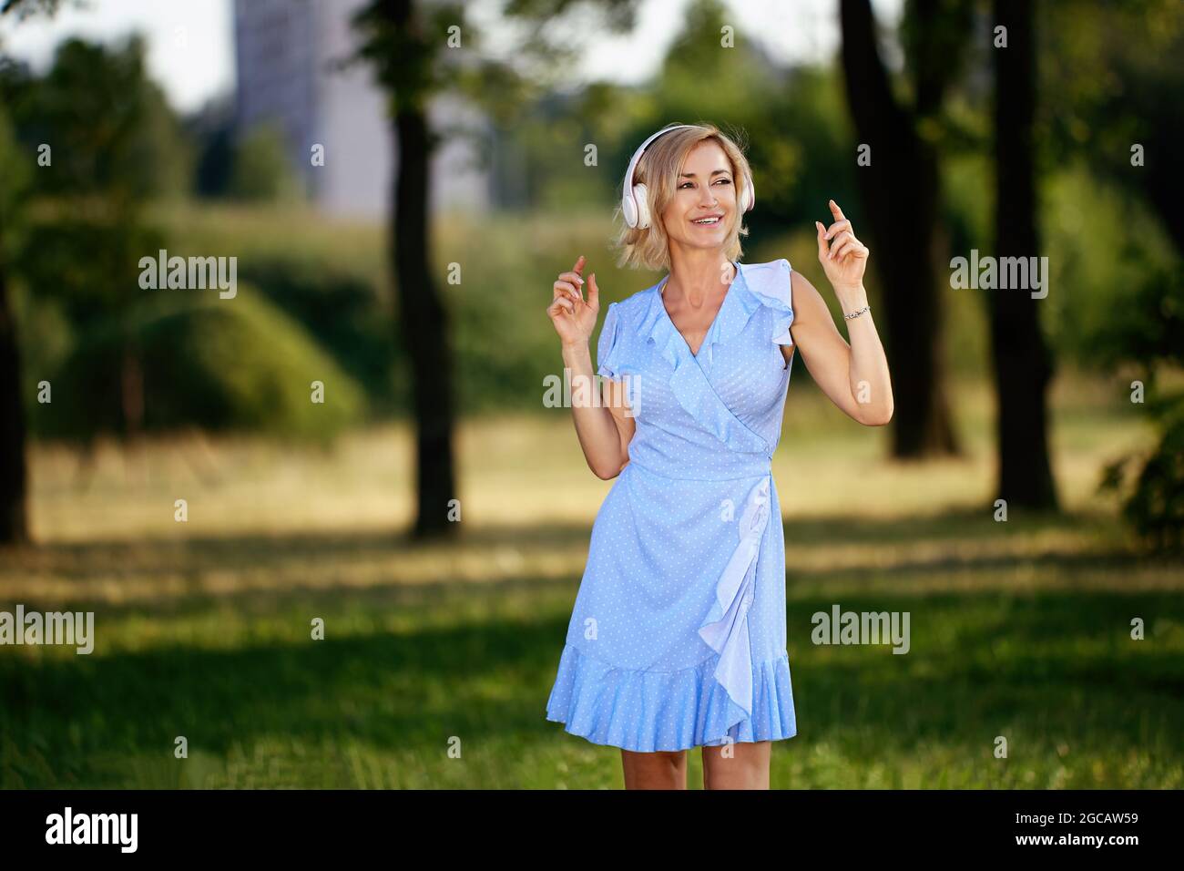 Donna felice in cuffie senza fili si trova nel giardino della città. Foto Stock