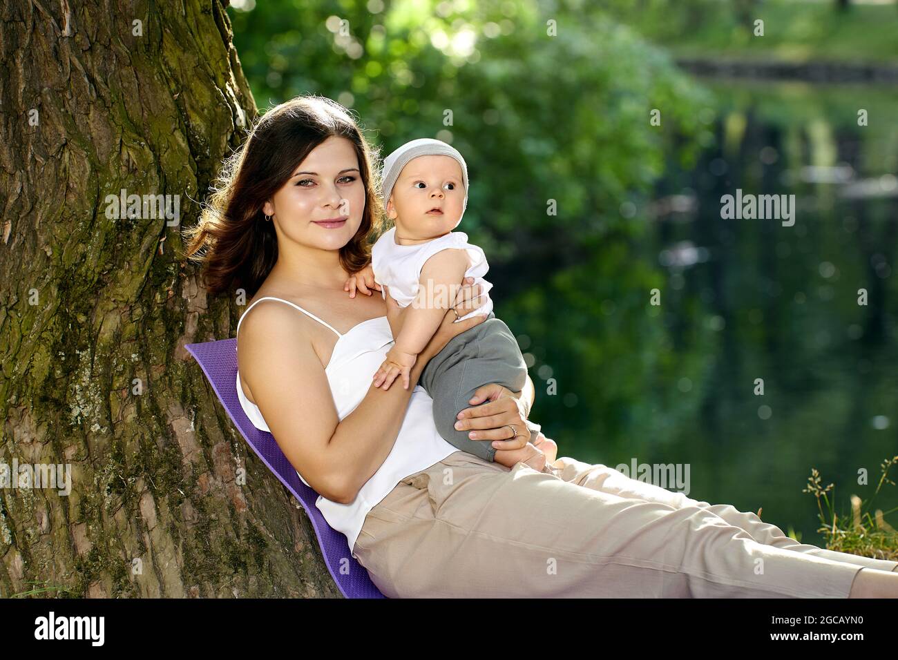 Donna con bambino piccolo hanno riposo nel parco pubblico vicino stagno. Foto Stock
