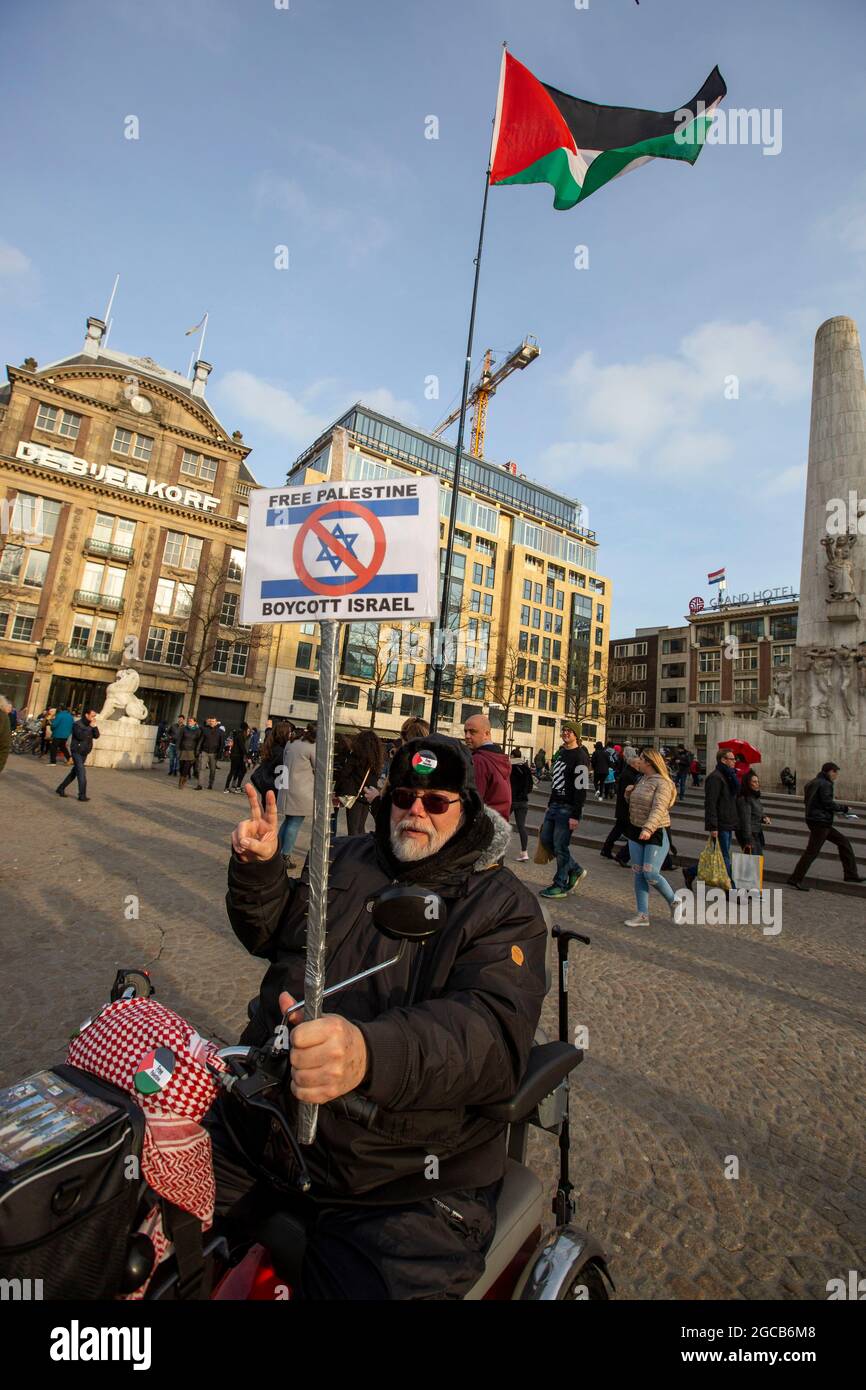 Un protestore detiene una bandiera palestinese e un cartello a Piazza Dam, Amsterdam, Paesi Bassi Foto Stock