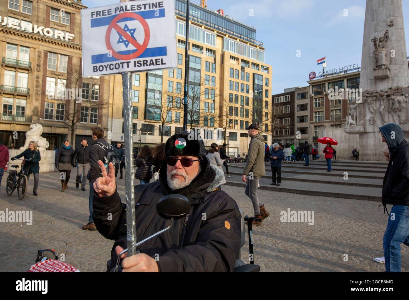 Un protestore detiene una bandiera palestinese e un cartello a Piazza Dam, Amsterdam, Paesi Bassi Foto Stock