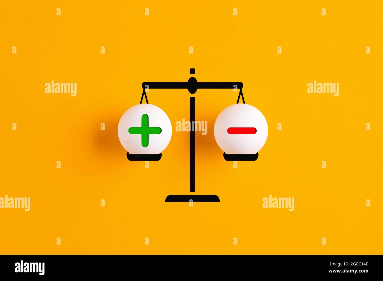 I simboli più e meno o positivo e negativo sono in equilibrio su una scala con sfondo giallo. Foto Stock