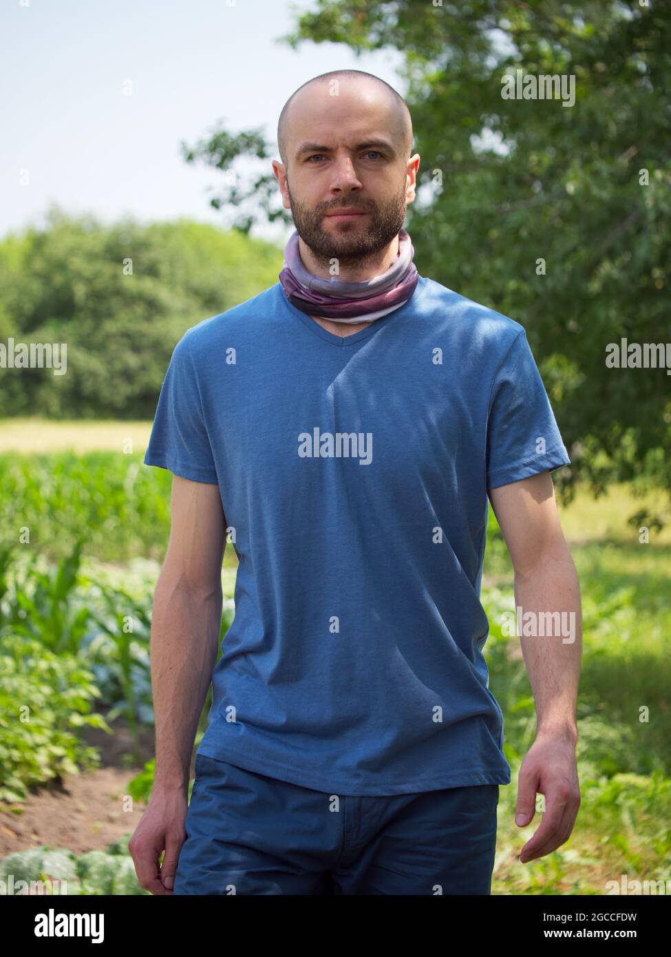 Un uomo calvo sicuro di sé con i capelli del viso cammina tra le piante in estate. Un look sicuro e deciso. Verticale. Foto Stock