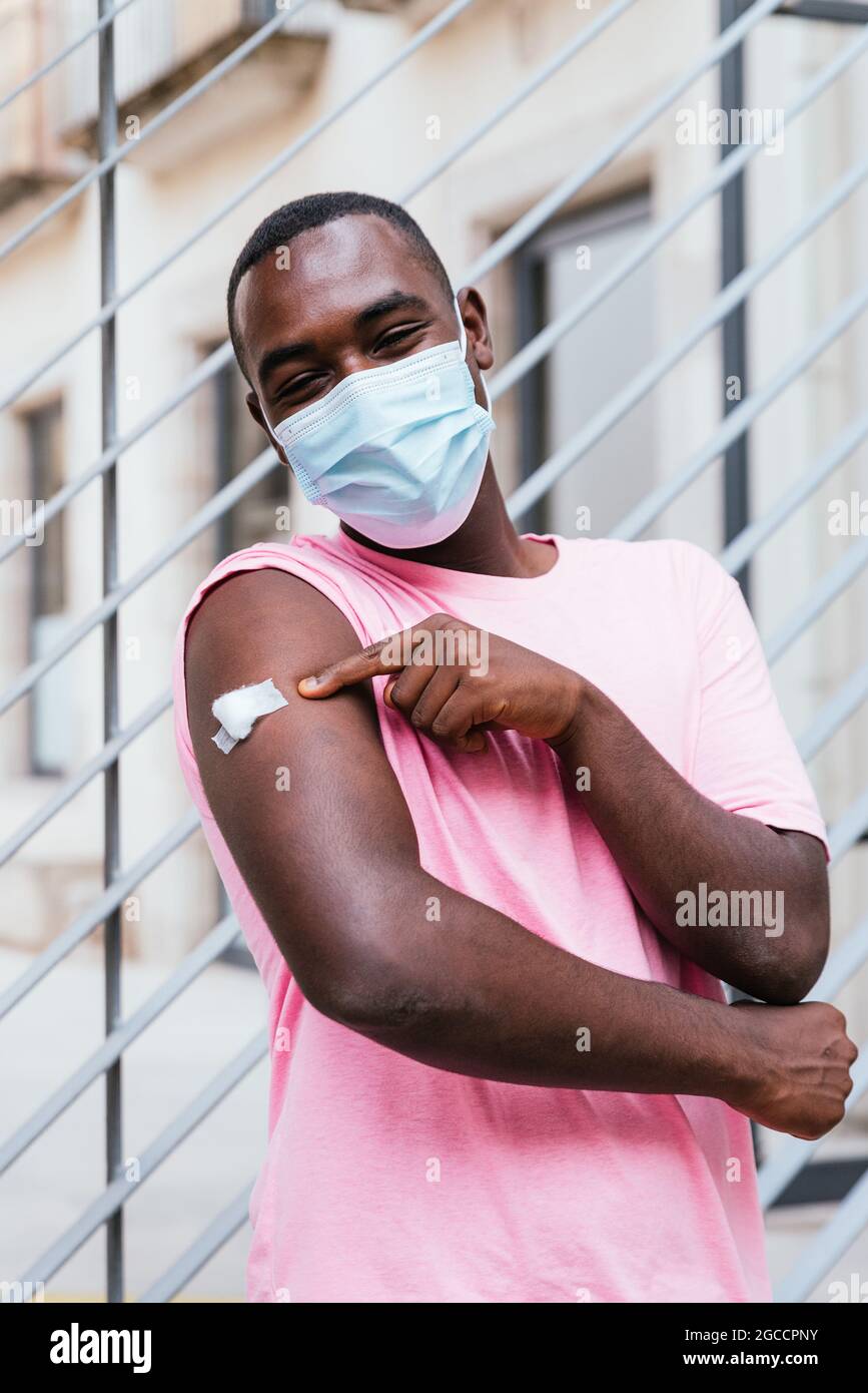 ritratto verticale di un giovane africano. È orgoglioso di mostrare il braccio dopo la vaccinazione Foto Stock