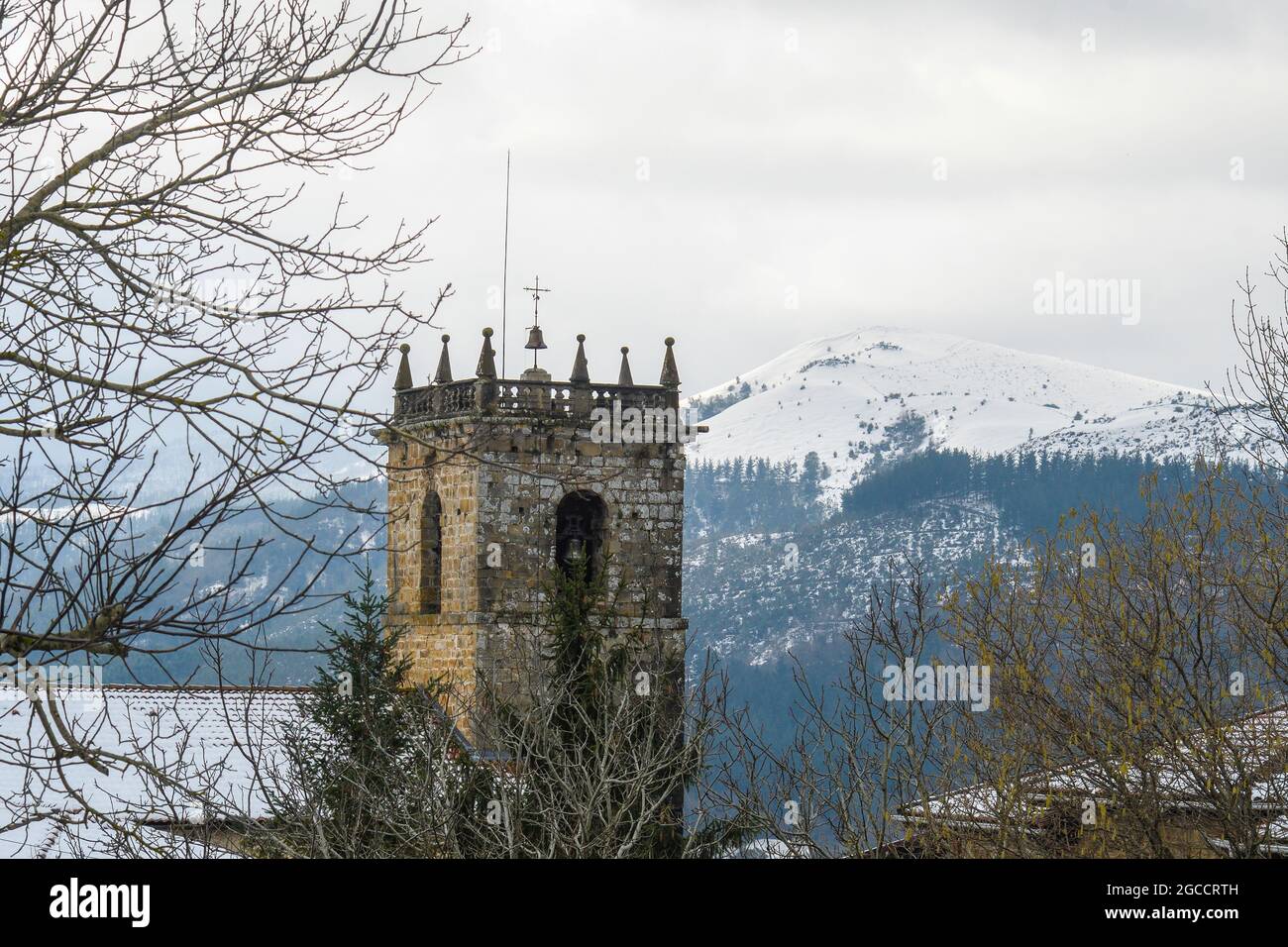 Campanile della chiesa di San Miguel de Linares ad Artzentales, Bizkaia, con le montagne innevate sullo sfondo. Foto Stock