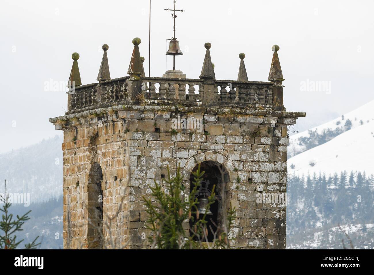 Campanile della chiesa di San Miguel de Linares ad Artzentales, Bizkaia, con le montagne innevate sullo sfondo. Foto Stock