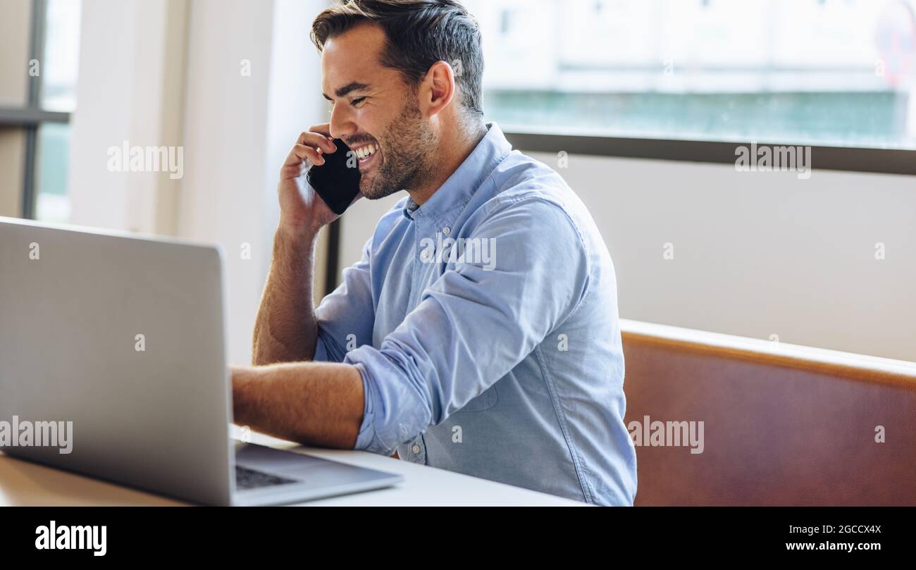 Libero professionista che chiama il cliente sul cellulare alla scrivania dell'ufficio. uomo d'affari seduto e felice mentre parla con uno smartphone in ufficio. Foto Stock