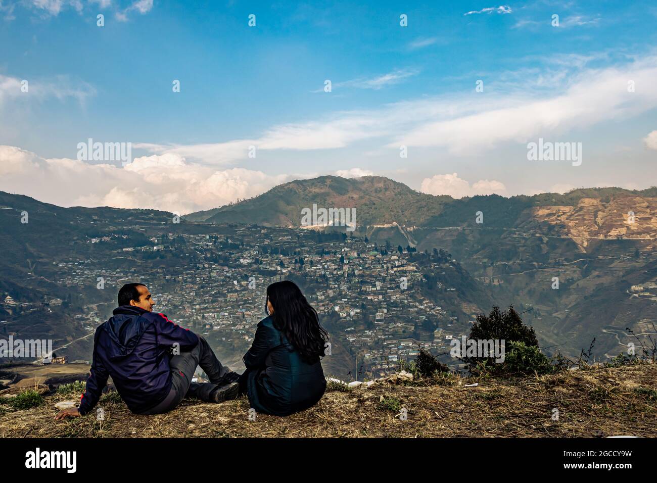 la coppia che siede sul bordo superiore della montagna con la struttura affollata della città e il cielo stupefacente alla sera immagine è presa al bomdiere arunachal pradesh india. Foto Stock