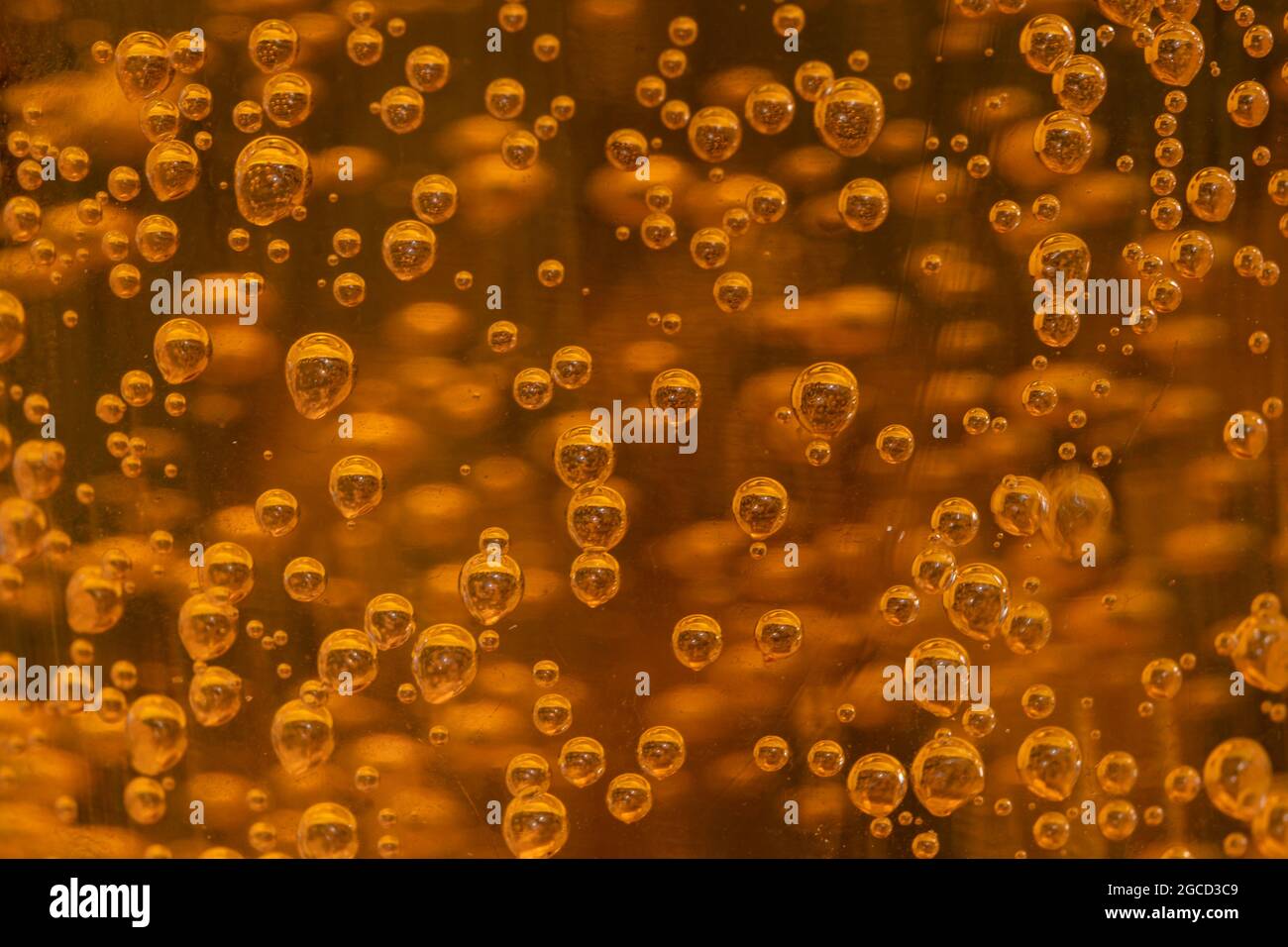 Bolle dorate che fluttuano nel liquido ambrato creando un motivo astratto Foto Stock