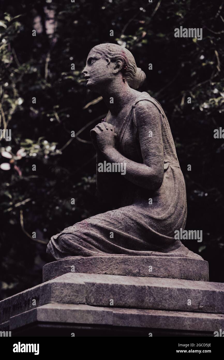 Statua in pietra di una figura inginocchiata in un tranquillo giardino Foto Stock