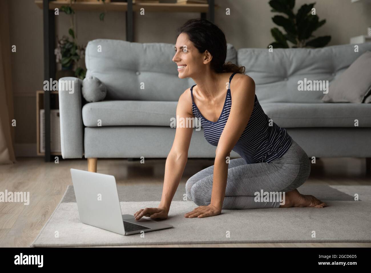 Donna sorridente e sognante in abbigliamento sportivo con laptop, in attesa di allenamento Foto Stock