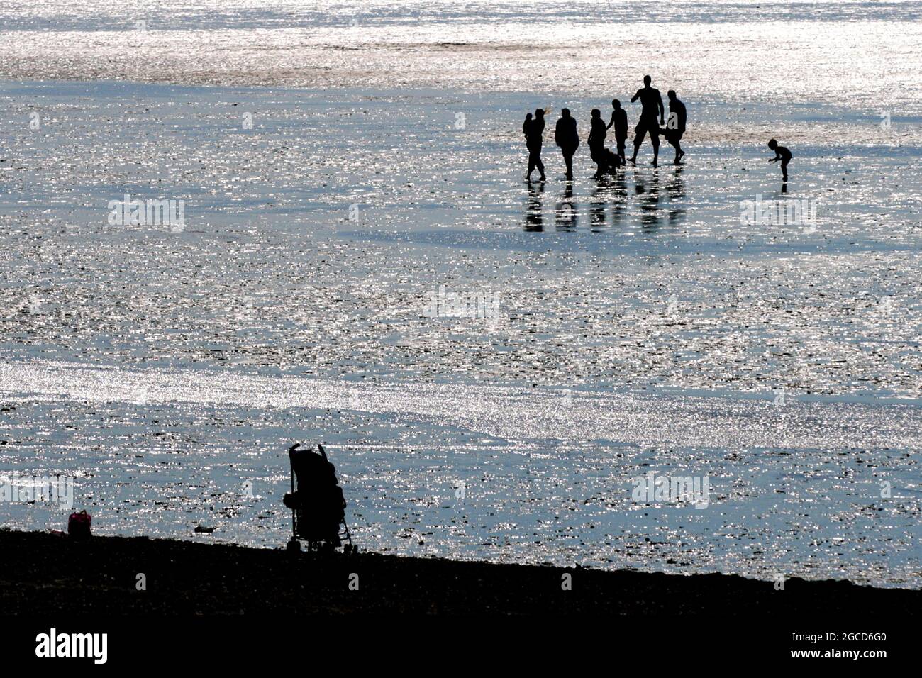 Famiglia in acqua in silhouette, Norfolk con una sedia a spinta o passeggino abbandonato sulla sabbia Foto Stock Famiglia in acqua in silhouette, Norfolk con una sedia a spinta o passeggino abbandonato sulla sabbia Foto Stock