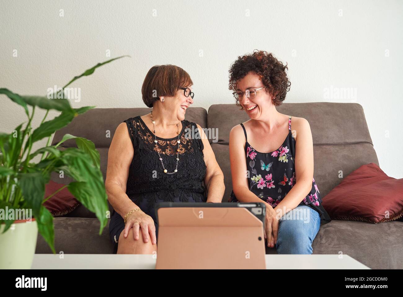 Una giovane donna e la sua madre anziana ridono mentre guardano i contenuti online tramite tablet digitale Foto Stock