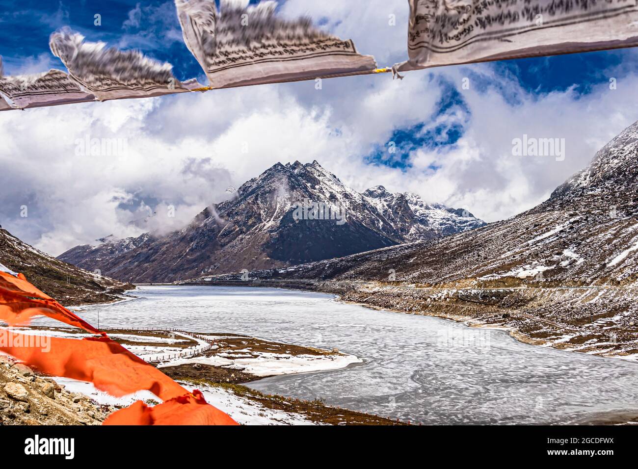 montagna con copertura della neve con cielo drammatico attraverso il blurred buddismo bandiere cornice al giorno l'immagine è presa al passo di sela tawang arunachal pradesh india. Foto Stock