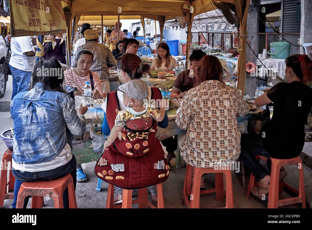 Madre con bambino portato in un imbragatura posteriore e mangiare in un ristorante all'aperto. Thailandia S. E. Asia Foto Stock