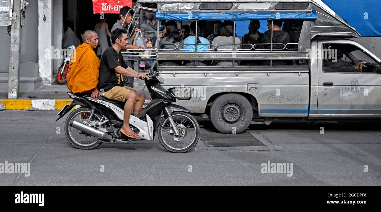 Thailandia modalità di trasporto con e monk su una moto che passa un songthaew baht bus pieno di passeggeri. Sud-est asiatico Foto Stock