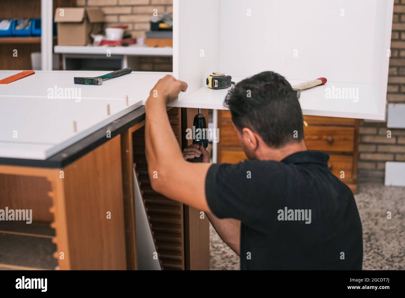 Lavoratore utilizzando un trapano per costruire un arredamento da cucina Foto Stock