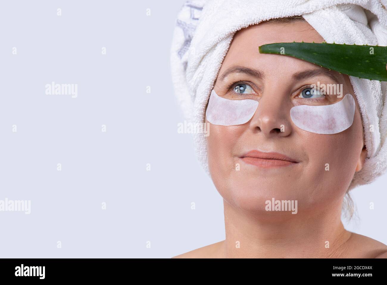 Donna moderna con perfette strisce cosmetiche applicate sulla pelle per palpebre inferiori e foglie di aloe che si prendono cura della pelle del viso. Foto Stock