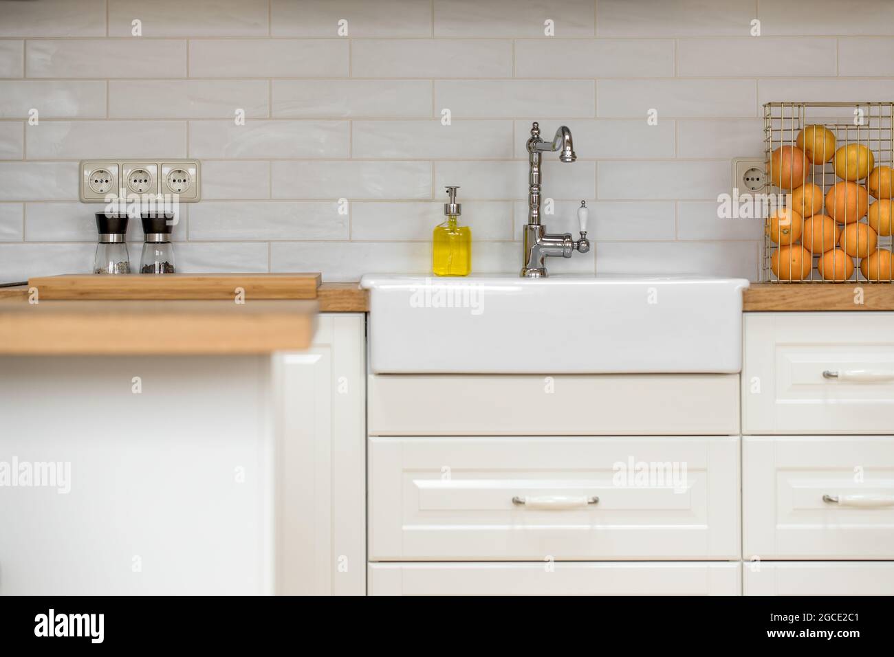 Primo piano della facciata in legno bianco di una cucina tradizionale in stile bianco con piastrelle metropolitane e piano di lavoro in legno massiccio Foto Stock