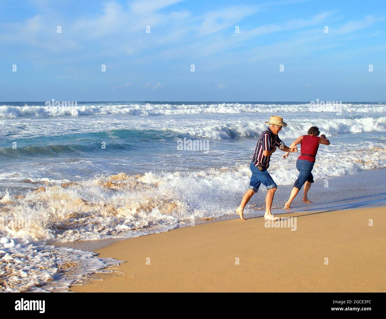 Marito e moglie corrono le onde su Polihale Beach sull'isola di Kauai, Hawaii. Ognuno corre in una direzione diversa. Foto Stock