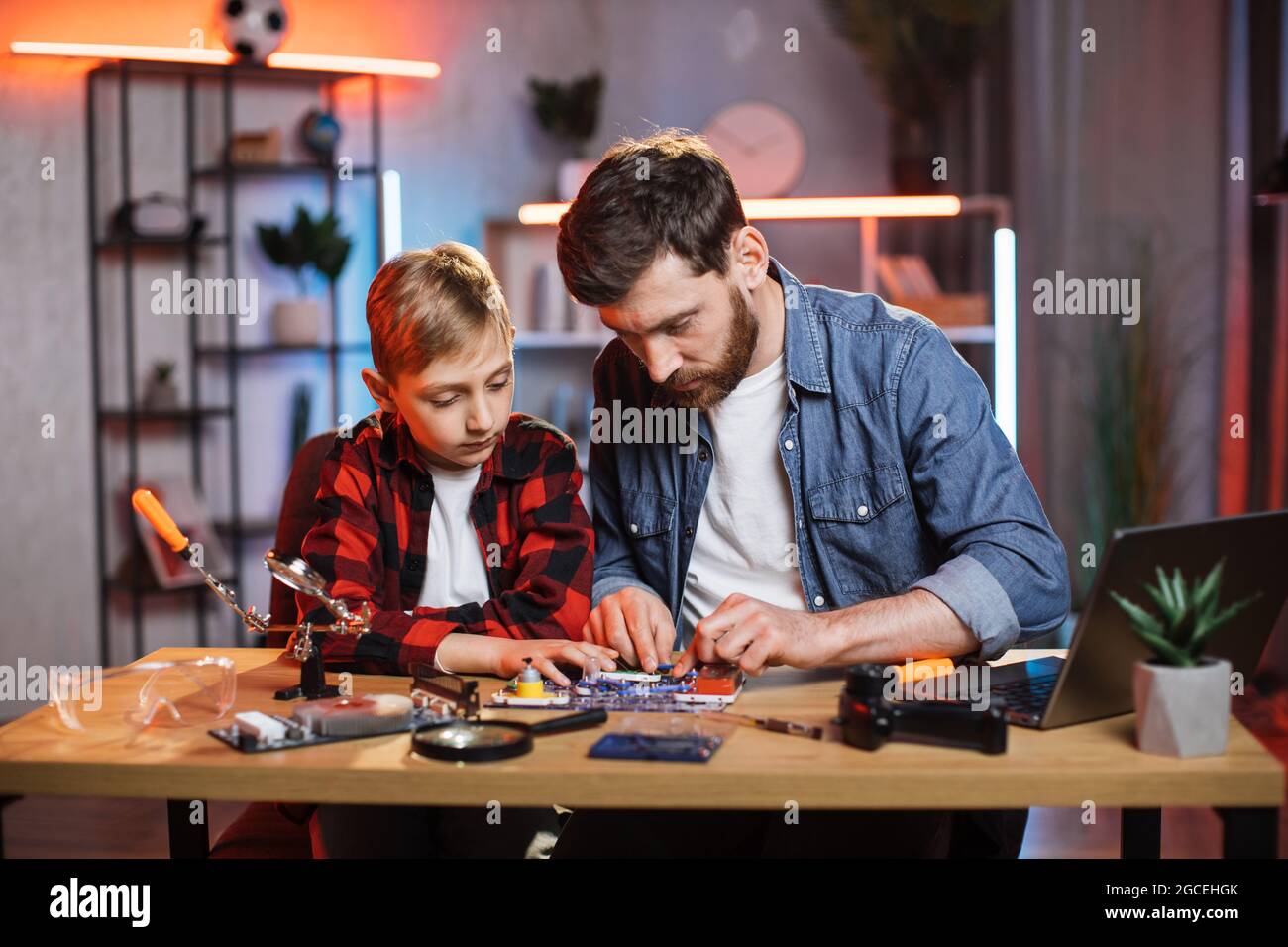 Bell'uomo beared e ragazzino usando il bambino designer per fare un semplice circuito elettrico. Giovane padre insegna al figlio facendo esperimenti di fisica a casa. Foto Stock