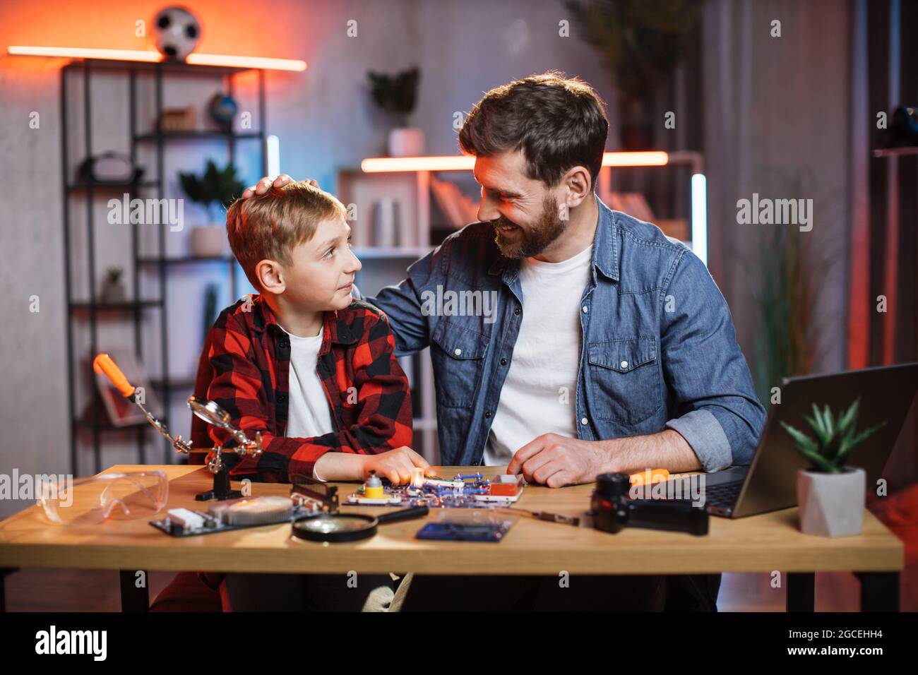 Felice giovane papà seduto con il suo figlio carino a tavola e facendo un semplice circuito elettrico utilizzando il giocattolo designer. Concetto di educazione dei bambini e di genitorialità. Foto Stock