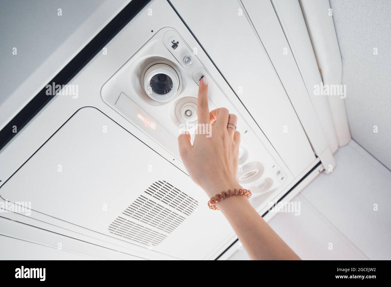 Il passeggero preme un pulsante sul pannello sopra la testa per accendere la ventola dell'aria condizionata e l'illuminazione all'interno dell'aeromobile Foto Stock