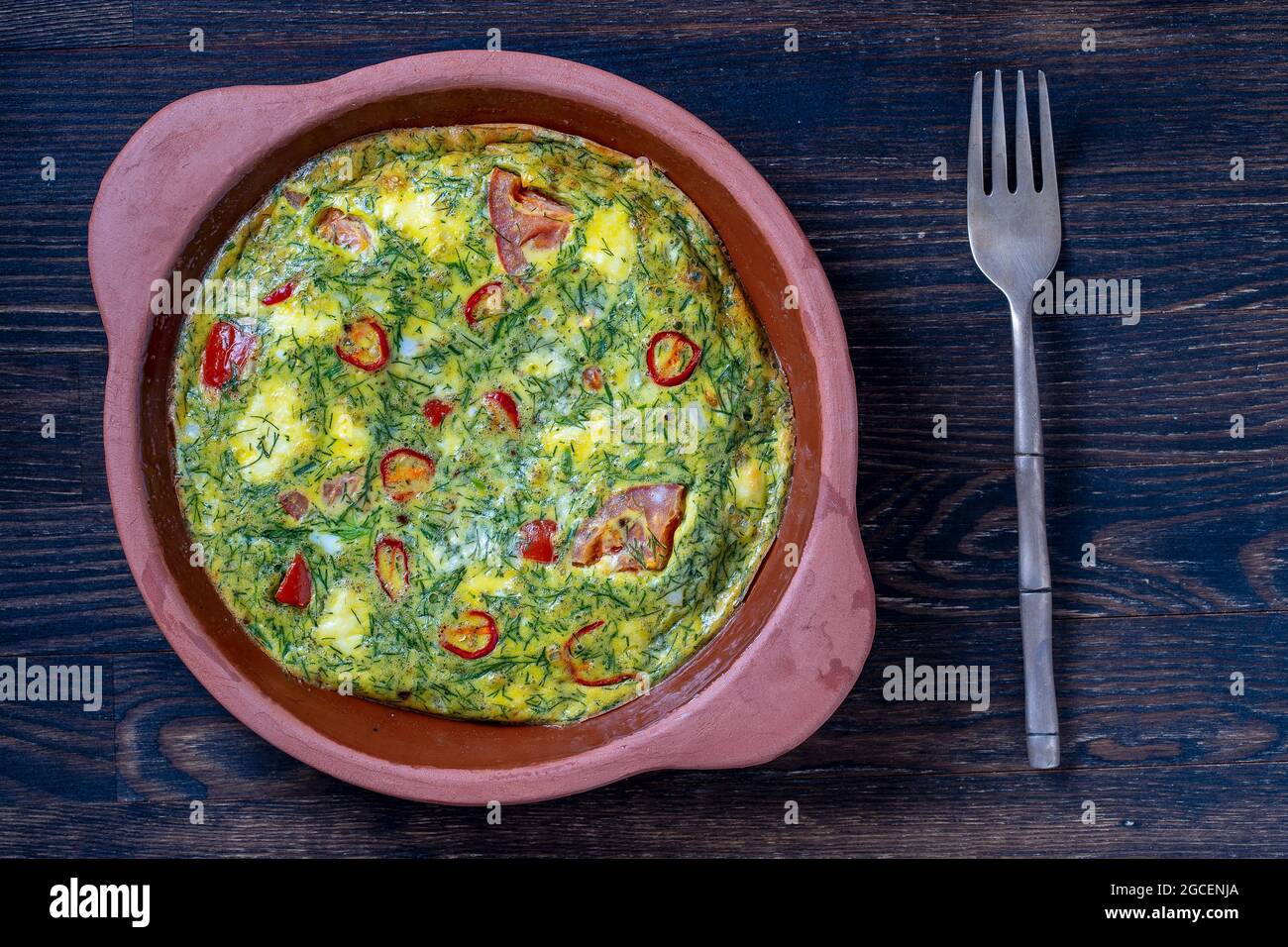 Ciotola in ceramica con frittata vegetale, semplice cibo vegetariano. Frittata con pomodoro, pepe, cipolla e formaggio feta su tavola di legno, primo piano. Italiano e. Foto Stock