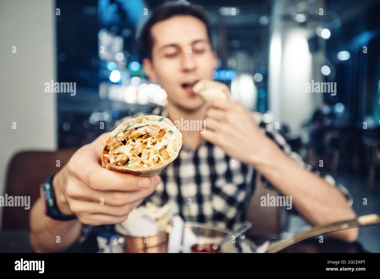 L'uomo europeo felice mangia i gyros greci o lo shawarma asiatico. La delicatezza del fast food è un rotolo di pane piatto con carne e verdure Foto Stock