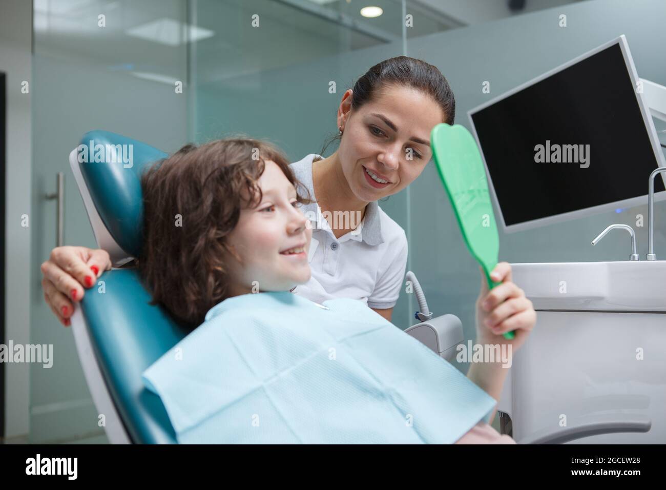 Adorabile ragazzo che controlla i denti nello specchio dopo la procedura dentale presso l'ufficio dei dentisti Foto Stock