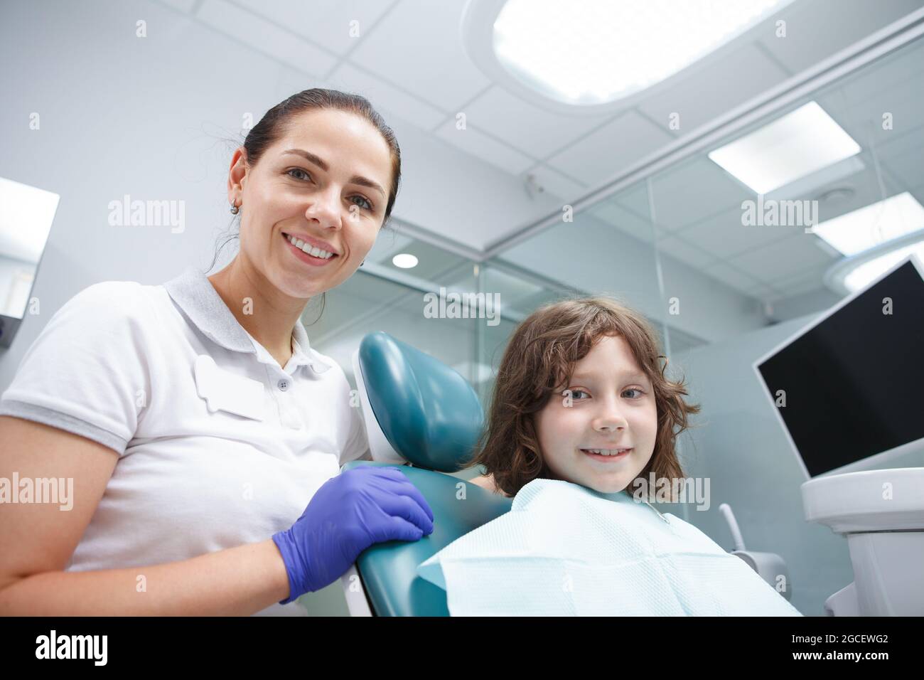 Bella dentista femminile e il suo giovane paziente sorridente alla macchina fotografica dopo il controllo dentale Foto Stock