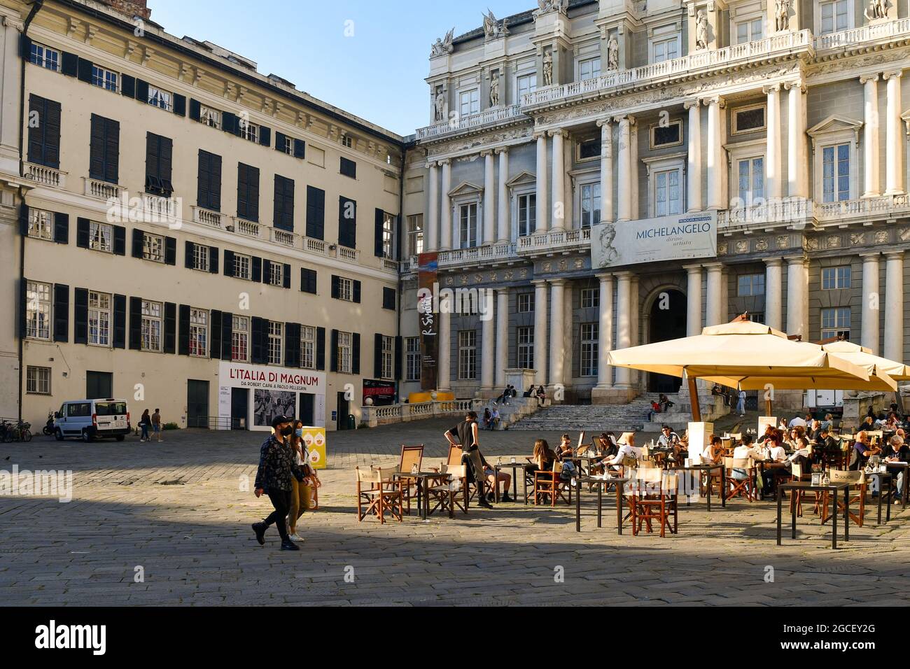 Persone sedute in un caffè all'aperto di fronte al Palazzo Ducale nel centro storico di Genova, Liguria, Italia Foto Stock