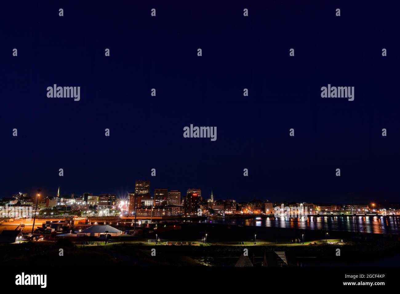 Saint John, NB, Canada - 1 agosto 2021: Guardando verso est lo skyline di San Giovanni di notte. La luce della città si riflette nel porto. Cielo blu scuro. Foto Stock
