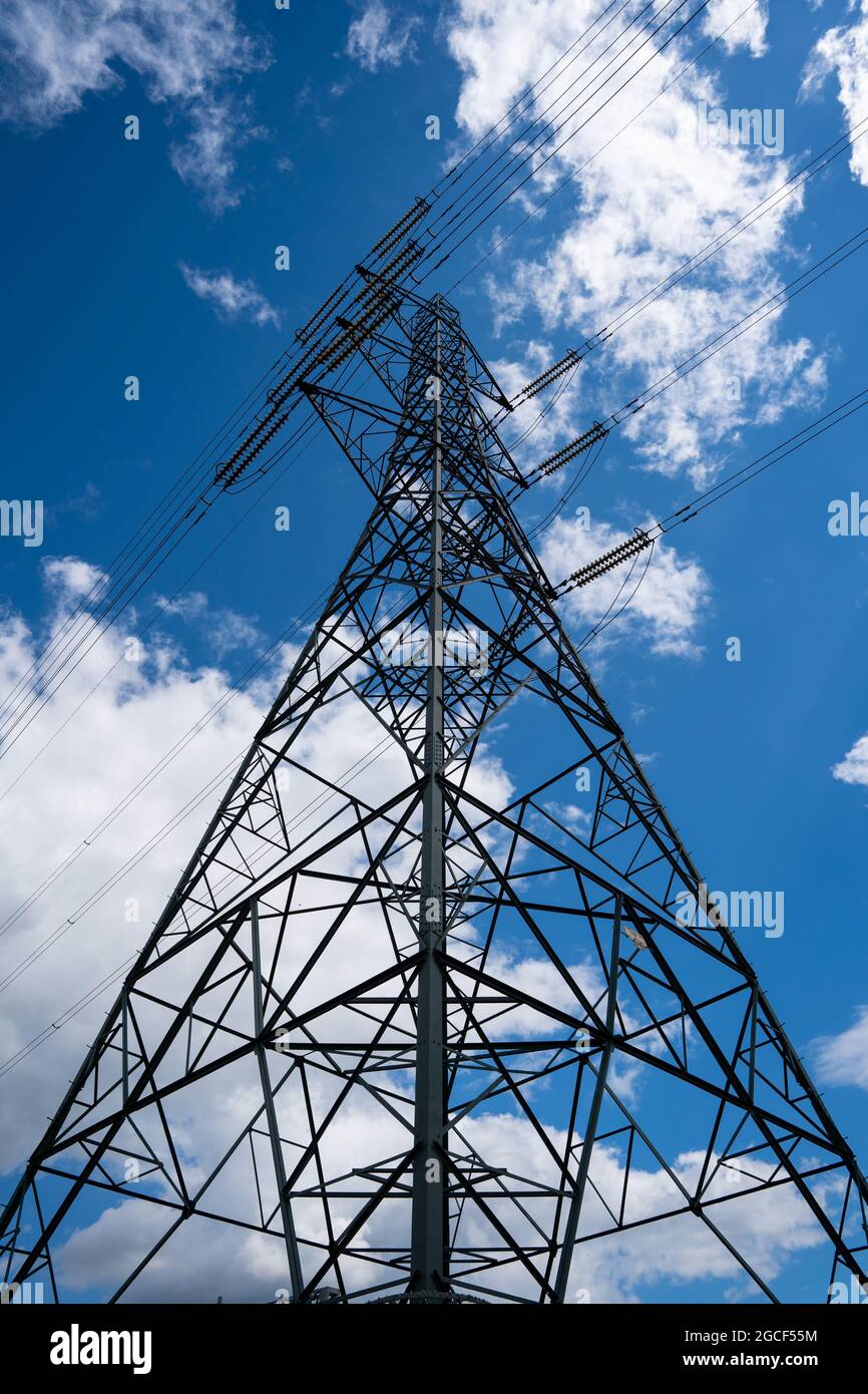 Traliccio elettrico con linee elettriche contro il cielo azzurro con nuvole bianche Foto Stock