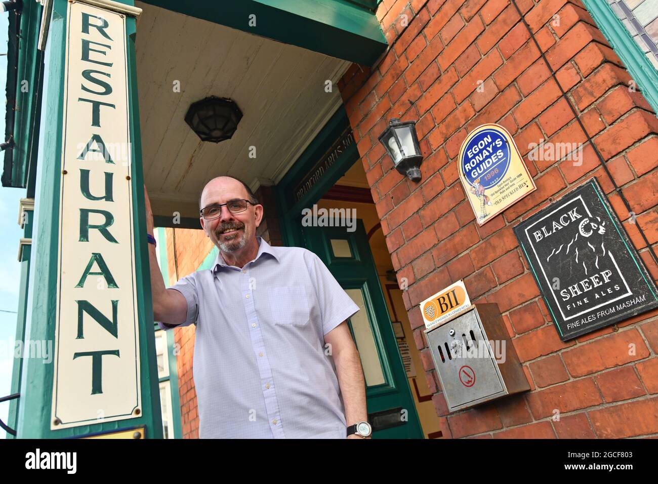 Llanymynech il villaggio che si trova a cavallo tra Inghilterra e Galles. Bob Hedley il padrone di casa dei Bradford Arms appoggiandosi sul suo portico che è in Galles mentre il suo pub è in Inghilterra. Foto Stock