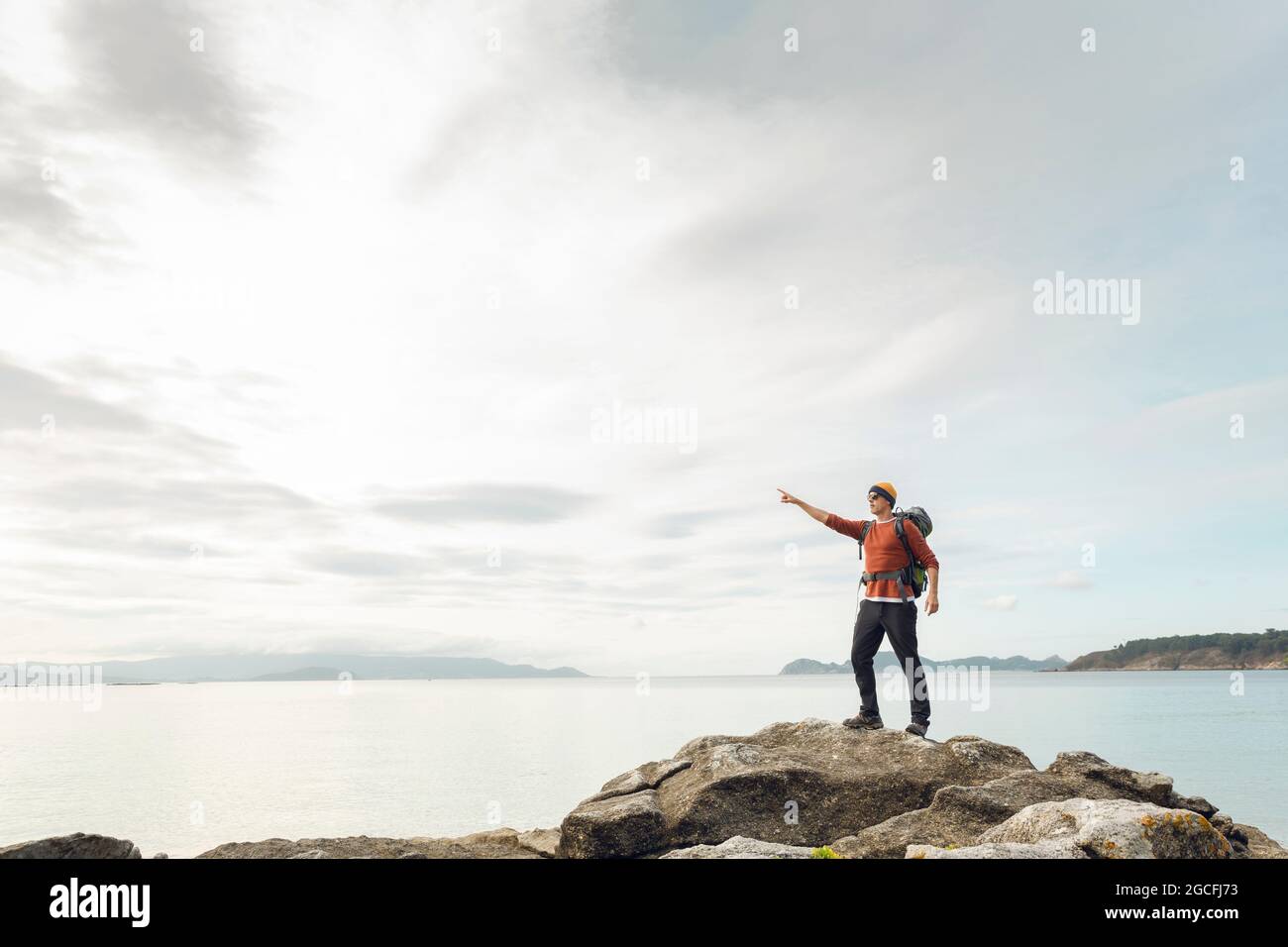 Uomo con zaino godendosi e puntando alla bella vista mattutina della costa Foto Stock