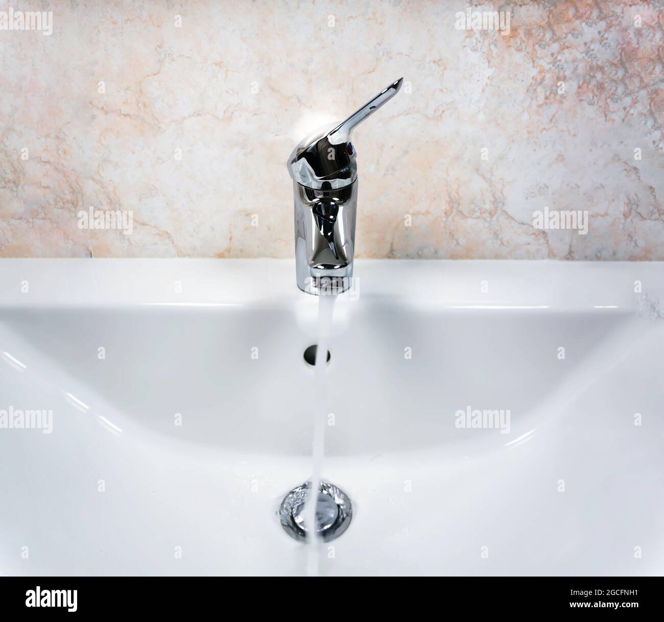 Rubinetto cromato con leva per mescolare acqua calda e fredda su un moderno lavandino bianco in un bagno con pareti piastrellate. Vita domestica e igiene Foto Stock