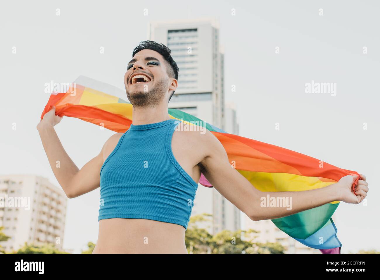 Giovane uomo gay ispanico che indossa bandiera multicolore in strada sensazione di felicità Foto Stock