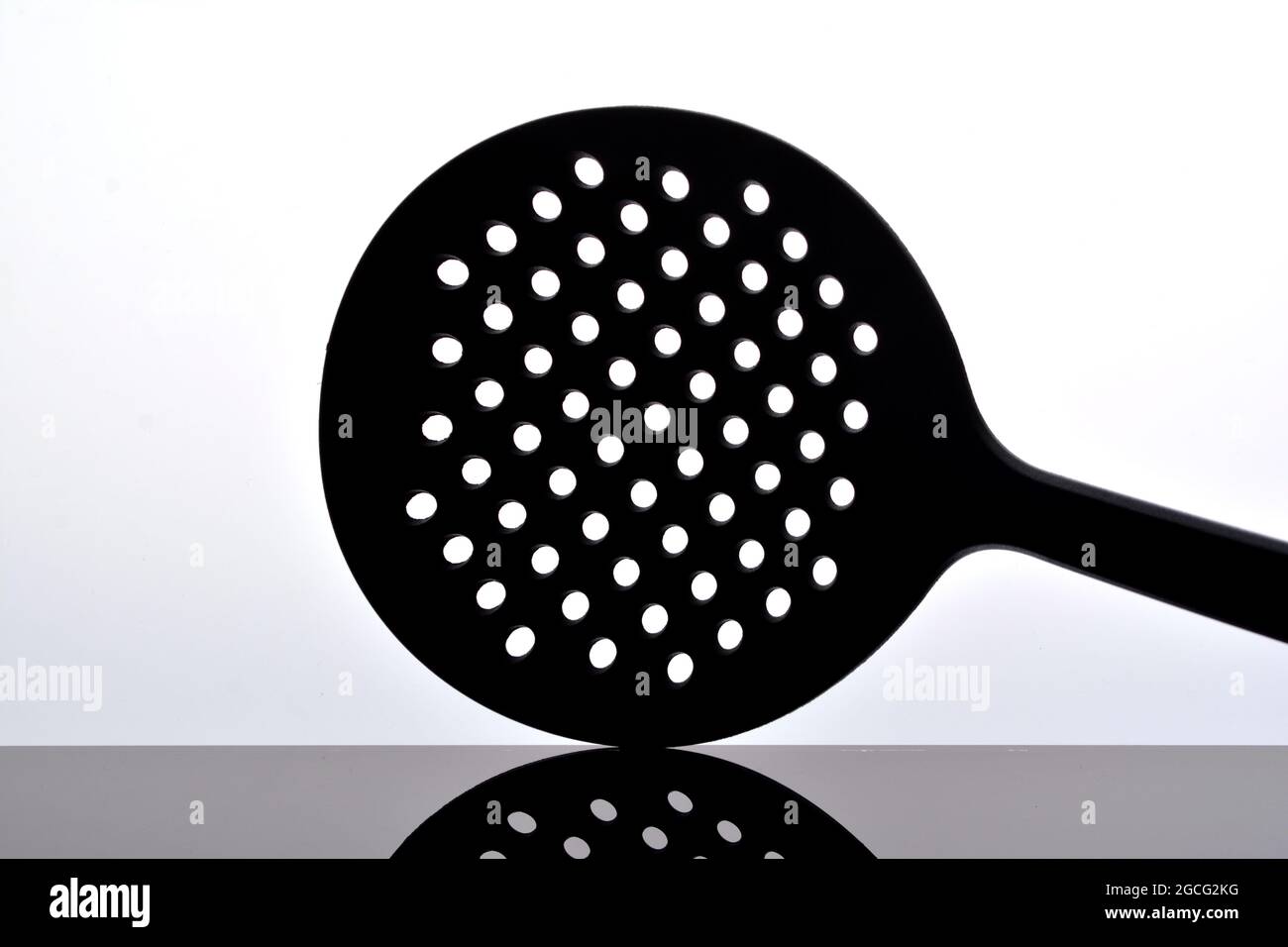 Skimmer, utensili da cucina isolati su bianco su superficie nera lucida con riflessi Foto Stock