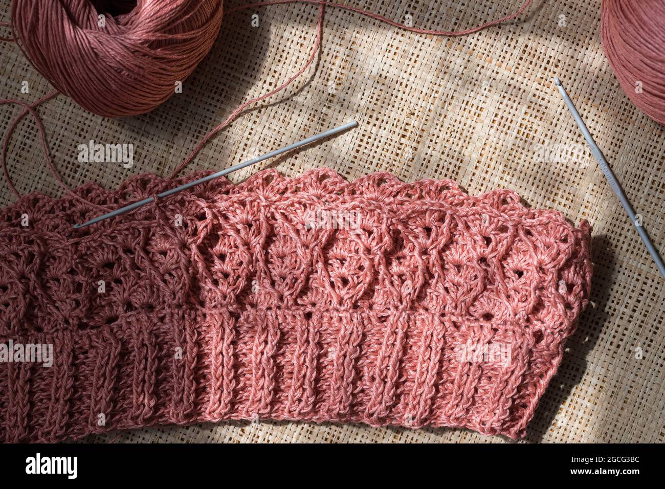 Pezzo di cucitura a catena di un abito rosa su uno sfondo a tela accanto a un paio di ganci a crochet. Foto Stock