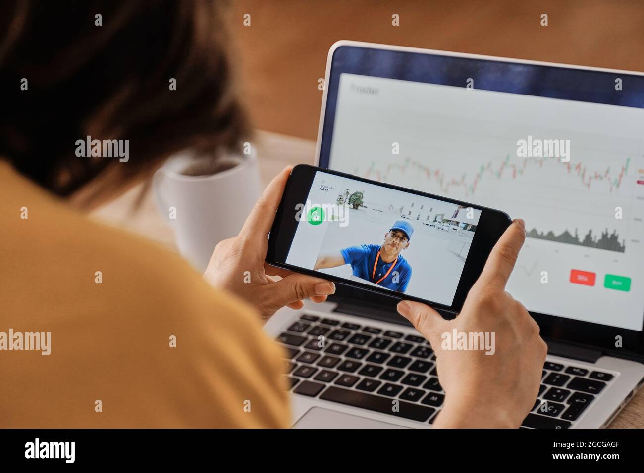 Donna che guarda il delivery man sulla telecamera di sicurezza video cctv sul telefono cellulare mentre lavora in ufficio a casa - Focus su smartphone Foto Stock