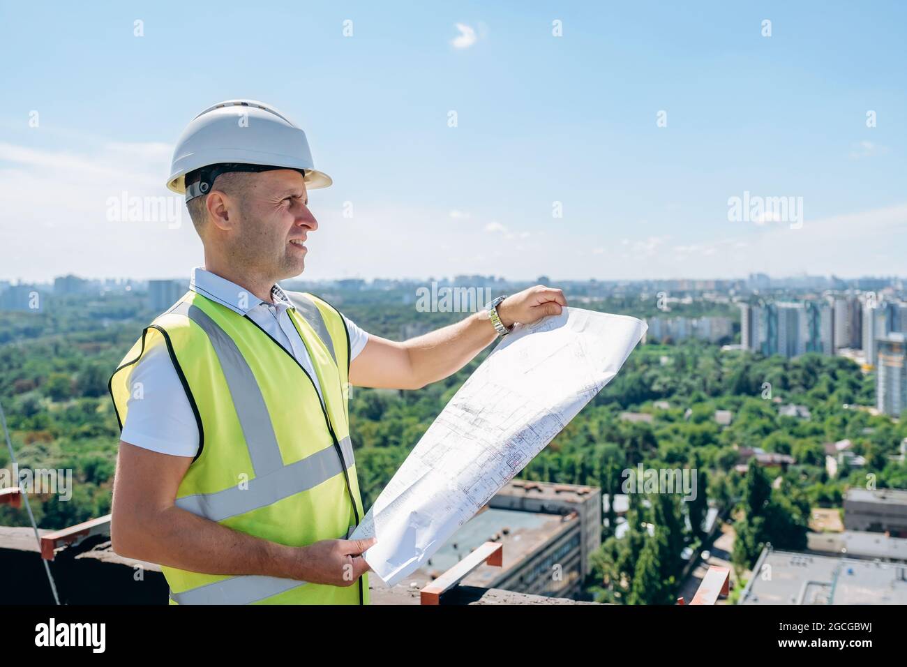 L'uomo in un casco bianco tiene il piano di costruzione e ispeziona il cantiere Foto Stock