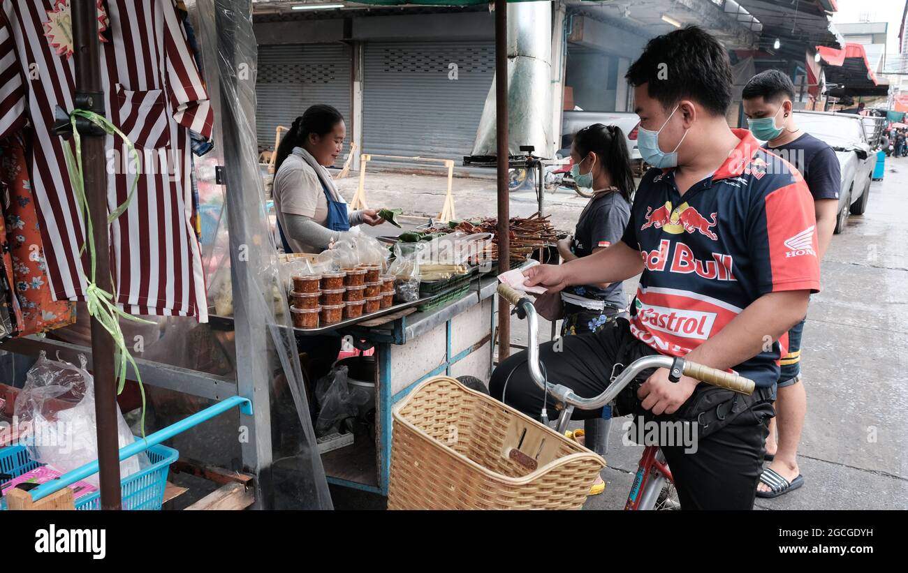 Uomo in bicicletta che indossa una maglia Racing Sport con contanti in mano al Klong Toey Market Bangkok Thailandia Foto Stock