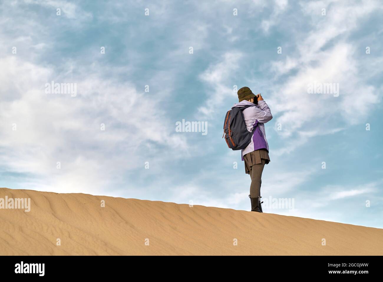 fotografa asiatica in piedi su una duna di sabbia scattando una foto Foto Stock